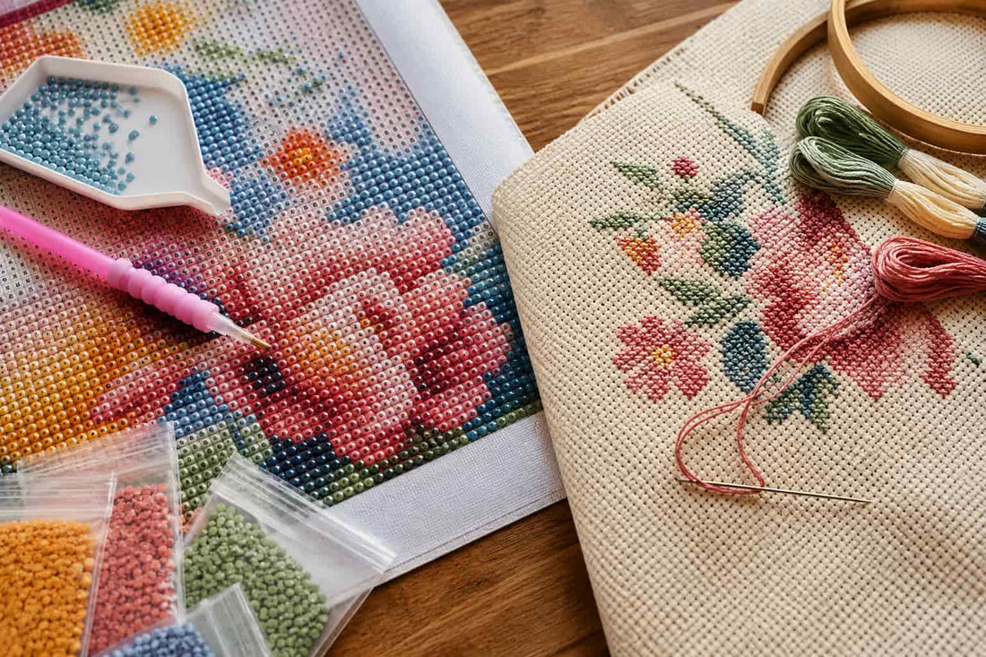 A close-up of a DIY diamond painting kit on a wooden table, showing a canvas with a floral design, beads, a pink-handled pick, and a finished embroidered fabric bag with matching thread and a wooden hoop.