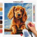 A diamond painting kit showing a dachshund puppy design, with a hand holding a pink paint tool. The image includes a color list chart on the right and a row of color beads on the left, all under the DrillinDazzle brand logo at the top.