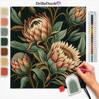 A diamond painting or cross-stitch style floral design on a white background, showing a hand holding a pink paint pen over the canvas. The artwork features large cream and peach protea flowers with green and brown leaves on a black ground.