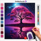 A diamond painting kit display featuring a completed fantasy tree-of-life canvas artwork in pink, purple, and blue tones, with a hand holding a pink pen tool at the lower right. The left side shows rows of color beads, and the top displays the brand name DrillnDazzle with a color chart on the right.