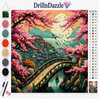 A diamond painting kit by DrillnDazzle featuring a scenic landscape design of a stone bridge over water surrounded by pink cherry blossoms, mountains, and a large moon. The image includes a color chart on the right, a row of paint pots and tools on the left, and the DrillnDazzle brand logo at the top.